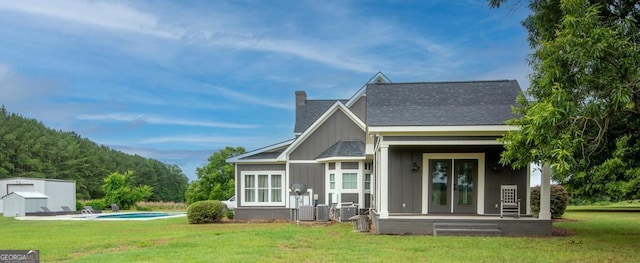 rear view of property featuring a shingled roof, an outdoor pool, a chimney, an outbuilding, and a yard