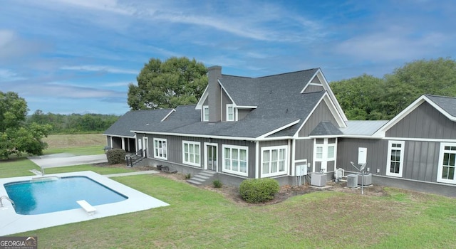 back of house with central AC, board and batten siding, a lawn, and an outdoor pool