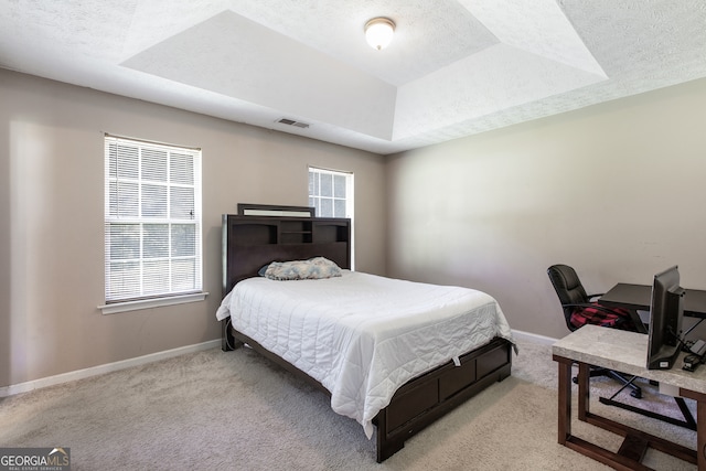 bedroom featuring light carpet, a textured ceiling, and a tray ceiling