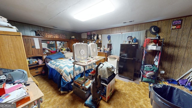 carpeted bedroom featuring wood walls and black refrigerator