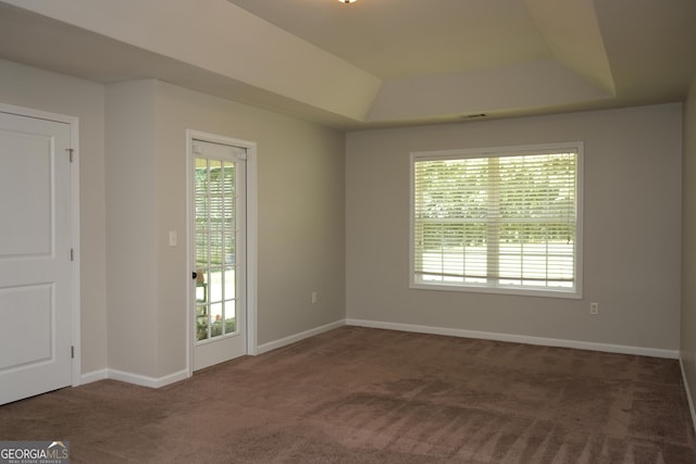 empty room with plenty of natural light, a tray ceiling, and dark colored carpet