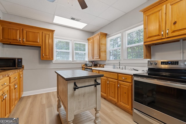 kitchen with ceiling fan, light hardwood / wood-style floors, a paneled ceiling, a skylight, and appliances with stainless steel finishes