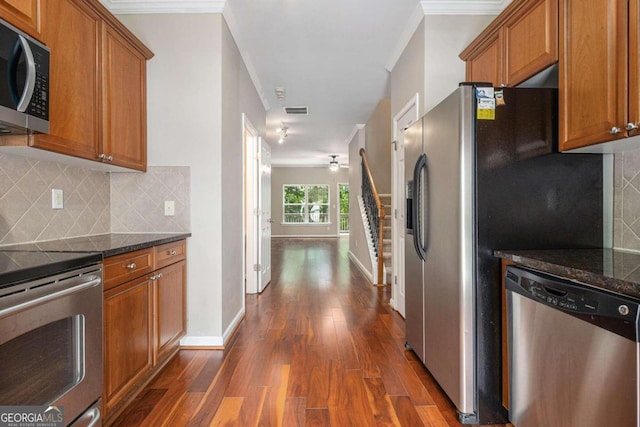 kitchen with backsplash, stainless steel appliances, crown molding, and dark stone countertops