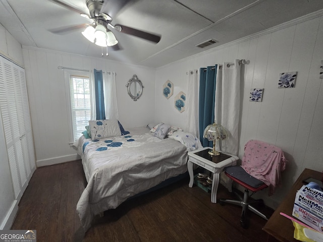 bedroom featuring a closet, ceiling fan, dark hardwood / wood-style flooring, and wood walls