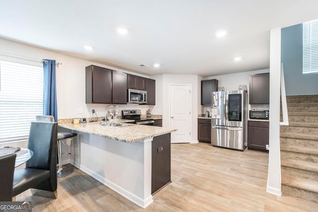 kitchen featuring light wood-type flooring, kitchen peninsula, light stone counters, stainless steel appliances, and sink