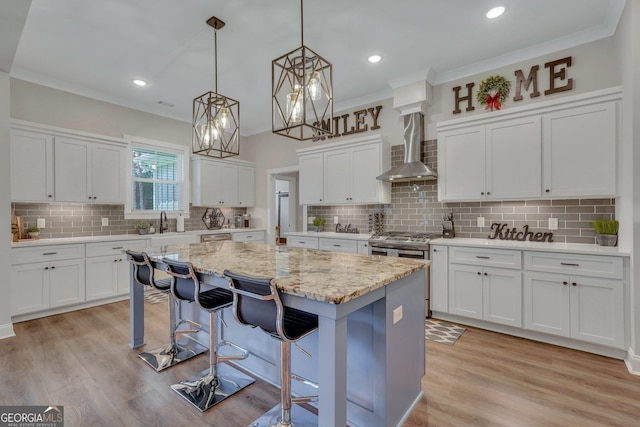 kitchen with white cabinets, hanging light fixtures, wall chimney exhaust hood, a kitchen island, and a breakfast bar area