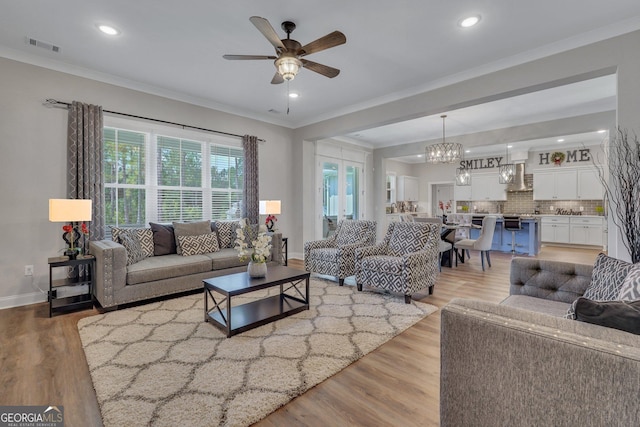 living room featuring ceiling fan with notable chandelier, light hardwood / wood-style floors, and crown molding