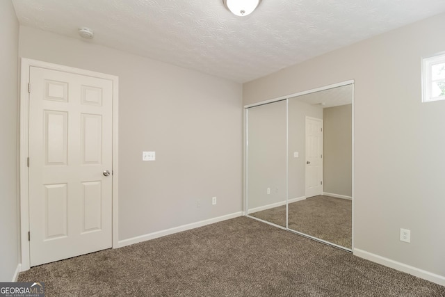 unfurnished bedroom with a closet, dark carpet, and a textured ceiling