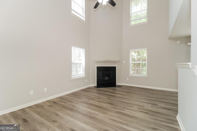 unfurnished living room featuring ceiling fan, a towering ceiling, and hardwood / wood-style flooring