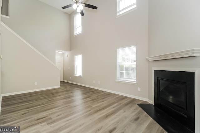 unfurnished living room with wood-type flooring, ceiling fan, a wealth of natural light, and a towering ceiling