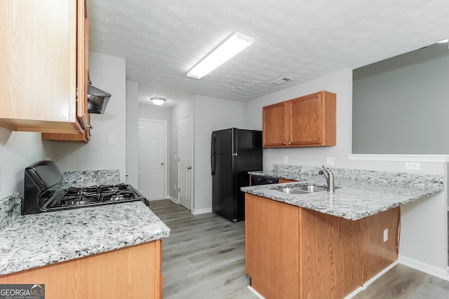 kitchen with black fridge, stove, kitchen peninsula, sink, and light wood-type flooring