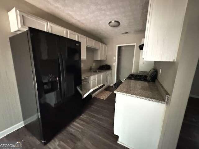 kitchen with white cabinetry, light stone countertops, dark hardwood / wood-style flooring, sink, and black refrigerator with ice dispenser