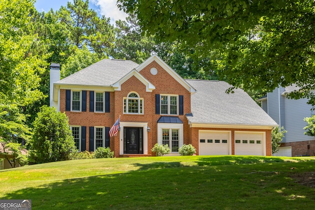 colonial house with brick siding, roof with shingles, a front yard, a chimney, and a garage