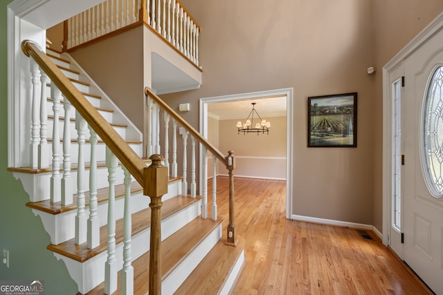 entrance foyer with light wood-type flooring, crown molding, a notable chandelier, and a high ceiling