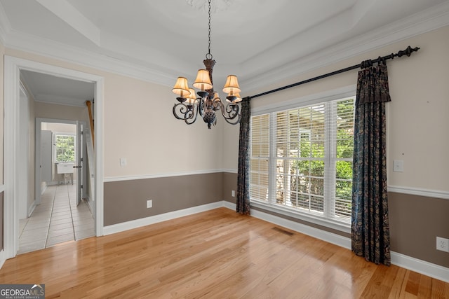 spare room with a raised ceiling, wood-type flooring, ornamental molding, and a chandelier