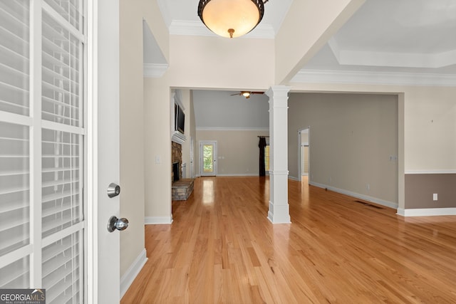 foyer featuring ceiling fan, a stone fireplace, decorative columns, light hardwood / wood-style floors, and ornamental molding