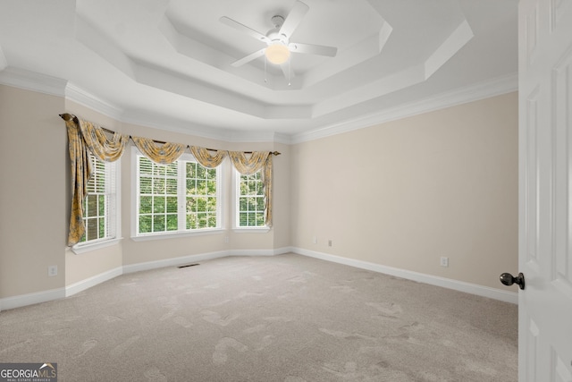 empty room featuring a raised ceiling, ceiling fan, light colored carpet, and ornamental molding