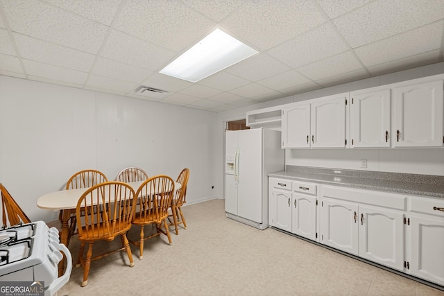 kitchen with white cabinets, a drop ceiling, and white refrigerator with ice dispenser