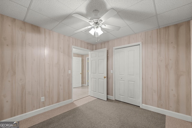 unfurnished bedroom with carpet, ceiling fan, a drop ceiling, and a closet