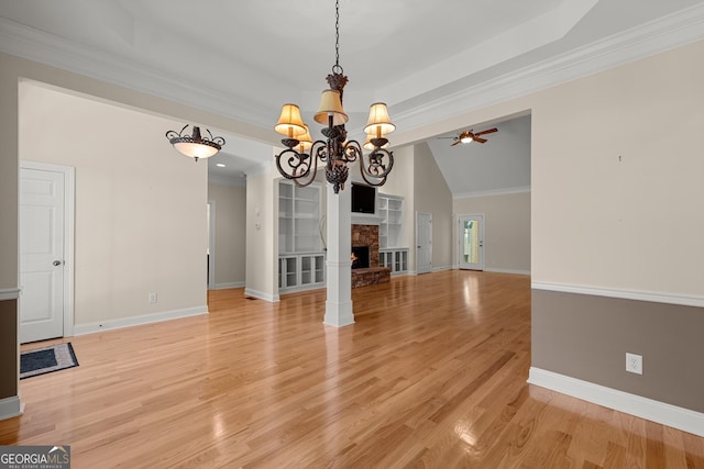 unfurnished living room featuring ceiling fan with notable chandelier, crown molding, a fireplace, and light hardwood / wood-style flooring