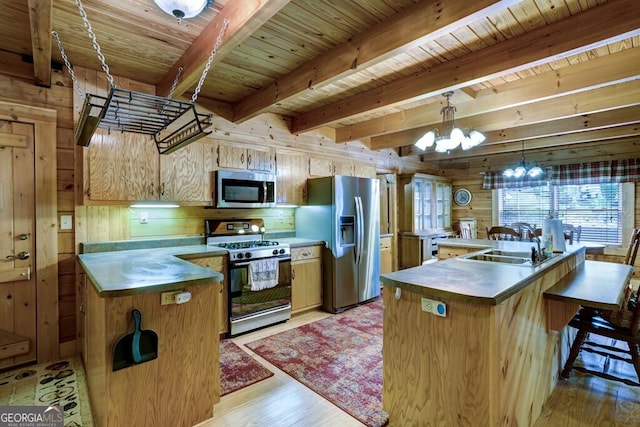 kitchen featuring wooden walls, a center island with sink, beamed ceiling, and appliances with stainless steel finishes