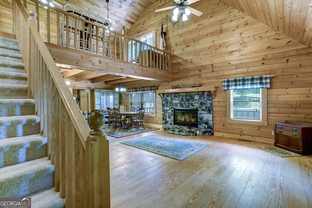 unfurnished living room featuring ceiling fan, high vaulted ceiling, a fireplace, hardwood / wood-style floors, and wood walls