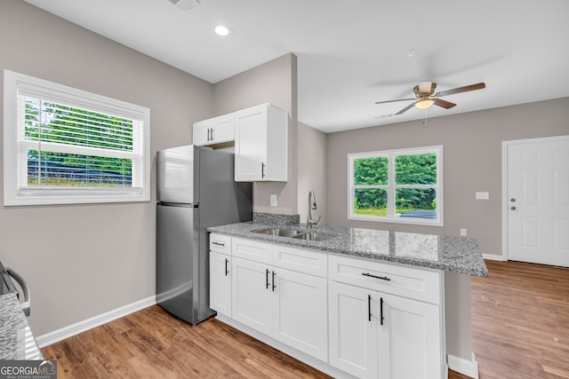 kitchen with white cabinetry, light wood-type flooring, sink, light stone countertops, and stainless steel refrigerator