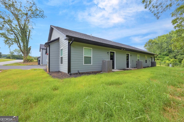 rear view of house with central AC and a lawn