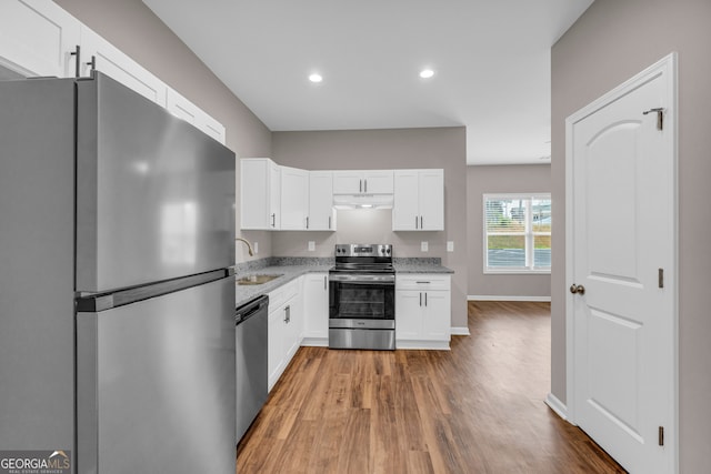 kitchen with white cabinetry, stainless steel appliances, light stone counters, and hardwood / wood-style floors