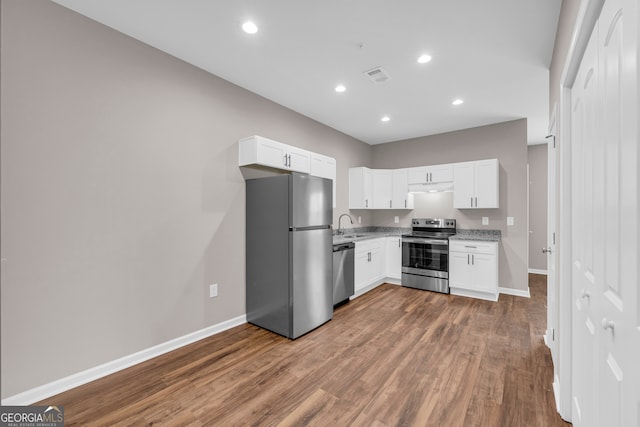 kitchen with white cabinetry, light stone counters, stainless steel appliances, and hardwood / wood-style floors