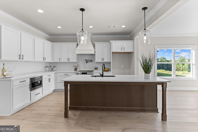 kitchen featuring premium range hood, white cabinetry, sink, and a center island with sink