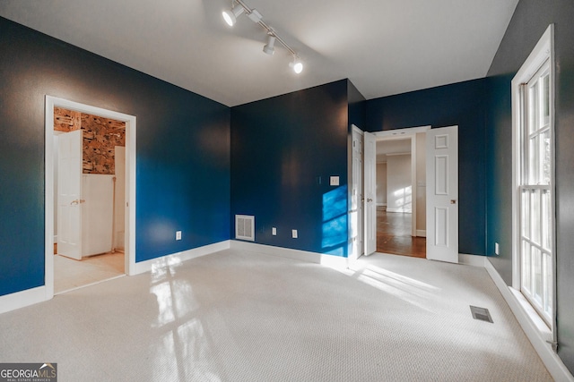 unfurnished bedroom featuring ensuite bathroom, light colored carpet, and rail lighting