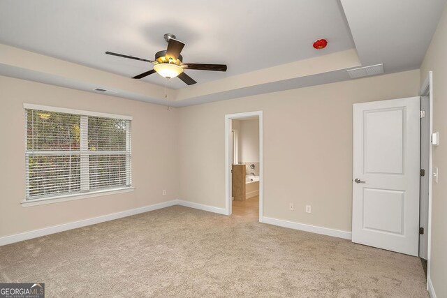 unfurnished bedroom with ensuite bathroom, ceiling fan, light carpet, and a tray ceiling