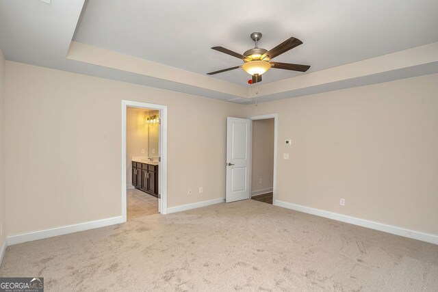 unfurnished bedroom featuring ceiling fan, a raised ceiling, light carpet, and ensuite bath