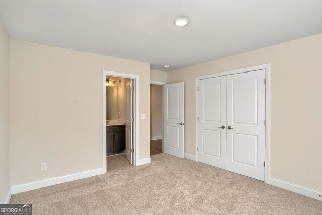 unfurnished bedroom with ensuite bathroom, light carpet, and a closet