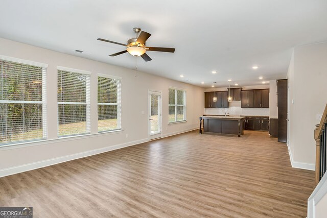 unfurnished living room with ceiling fan, sink, and light wood-type flooring