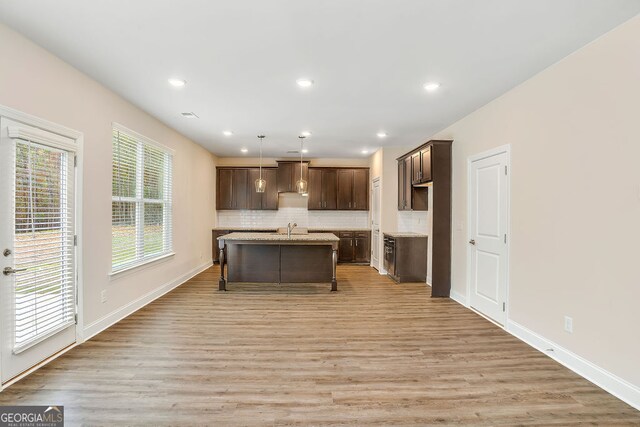 kitchen featuring decorative backsplash, light hardwood / wood-style floors, hanging light fixtures, and an island with sink