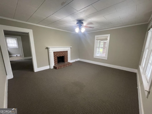 unfurnished living room with ceiling fan, dark carpet, crown molding, and a brick fireplace