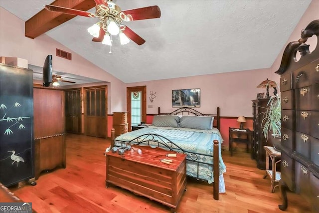 bedroom with a textured ceiling, wood-type flooring, ceiling fan, and vaulted ceiling with beams