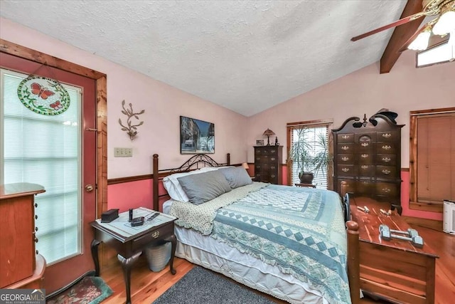 bedroom with lofted ceiling with beams, a textured ceiling, a ceiling fan, and wood finished floors