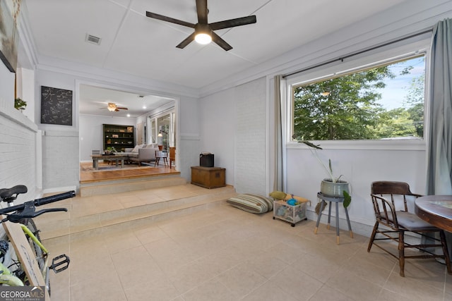 interior space with visible vents, a ceiling fan, brick wall, ornamental molding, and tile patterned floors