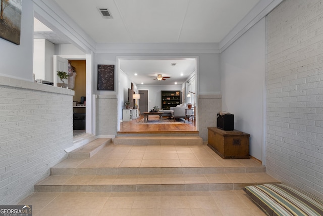 foyer entrance with brick wall, a ceiling fan, visible vents, and tile patterned floors