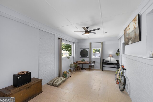 misc room featuring light tile patterned floors, ceiling fan, and brick wall