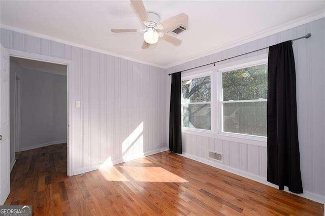 spare room featuring a ceiling fan, wood finished floors, visible vents, and crown molding