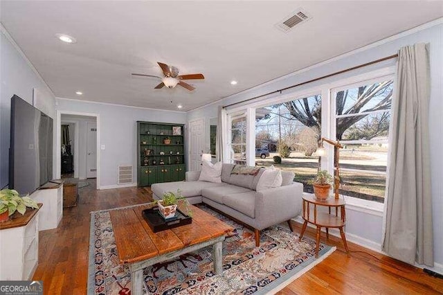 living area with ornamental molding, visible vents, baseboards, and wood finished floors