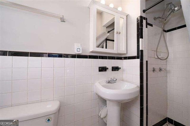 bathroom with tile walls, a wainscoted wall, a shower stall, and toilet