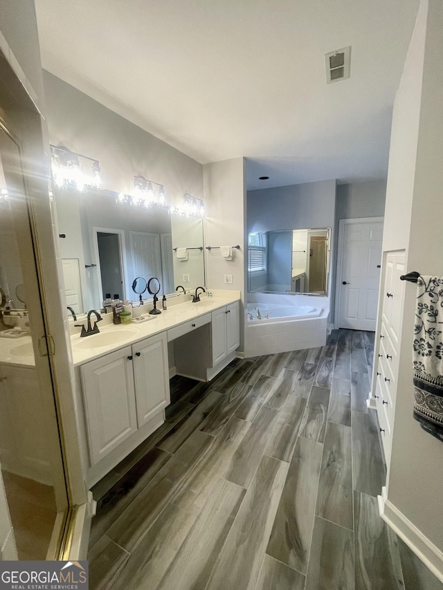 bathroom featuring wood finish floors, a garden tub, double vanity, visible vents, and a sink