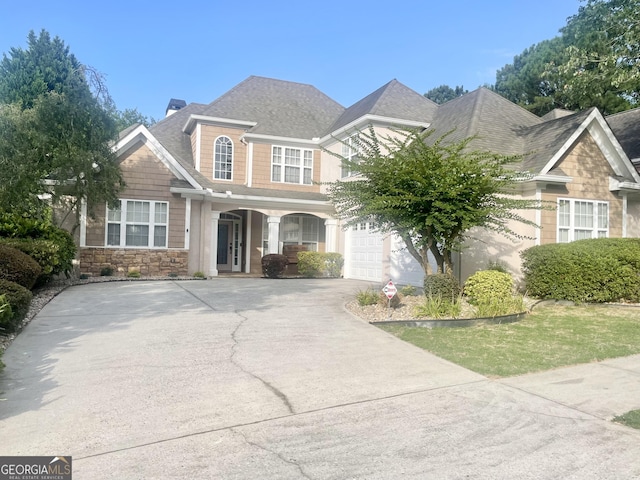 view of front facade with stone siding, a shingled roof, and driveway