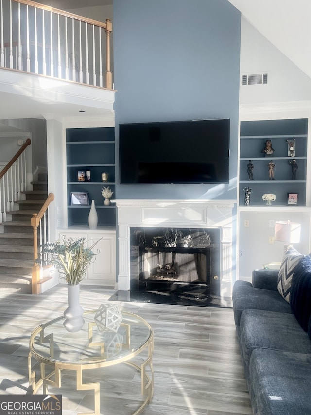 living area featuring visible vents, a towering ceiling, a premium fireplace, stairway, and wood finished floors