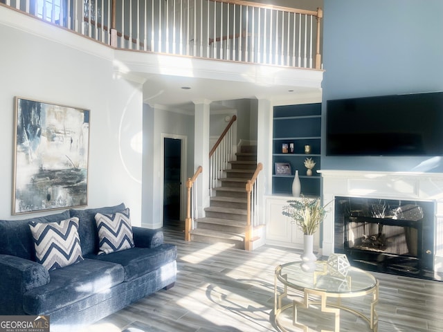 living area with a high ceiling, a premium fireplace, wood finished floors, stairs, and ornamental molding